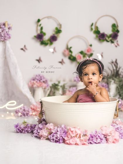A quiet moment of curiosity during a first birthday tub session. The purple and pink flowers create a whimsical, enchanted garden feel.