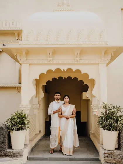 A serene and elegant portrait of the couple in beautiful white and gold traditional wear, standing in a classic archway.