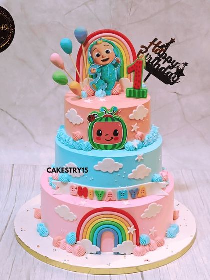A vibrant three-tier Cocomelon dream cake for a first birthday. This 5kg chocolate cake features colorful tiers, fondant rainbows, and the beloved Cocomelon baby character on top.