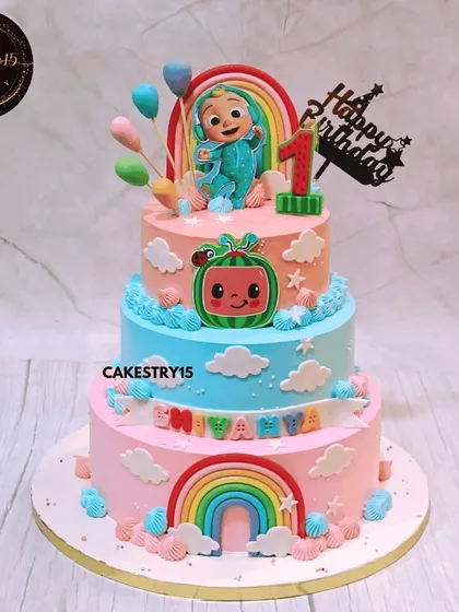 A vibrant three-tier Cocomelon dream cake for a first birthday. This 5kg chocolate cake features colorful tiers, fondant rainbows, and the beloved Cocomelon baby character on top.
