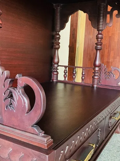 A close-up of the side of a custom mandir, highlighting the hand-carved peacock motif and the detailed railing. The rich mahogany finish adds to its traditional and elegant feel.