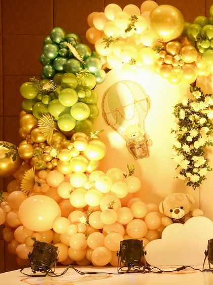 A detail shot of a balloon arch in shades of green, gold, and peach. The addition of hot air balloon cutouts and butterfly accents adds layers of detail to the 'We Can Bearly Wait' theme.