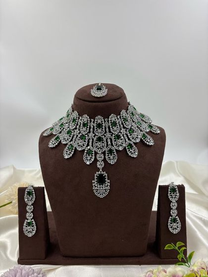 A full-coverage AD bridal set with a matching maang tikka. This silver-plated design is available in a wide range of colors like green, blue, pink, and white, making it a versatile choice for weddings.