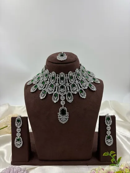 A heavy, full-collar AD necklace set with green stones and a matching maang tikka.