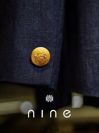 A close-up of a custom-embossed gold button on a navy blazer. These small, personalized details are what make a bespoke garment truly special.