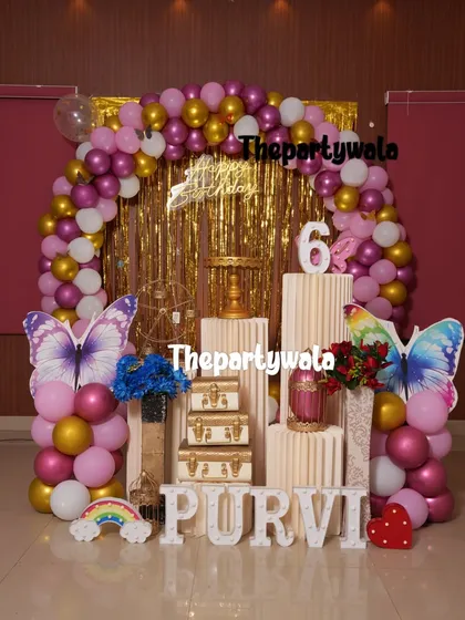 A glamorous butterfly theme with a gold shimmer backdrop. The magenta and gold balloon arch with large butterfly cutouts creates a very rich and celebratory look.