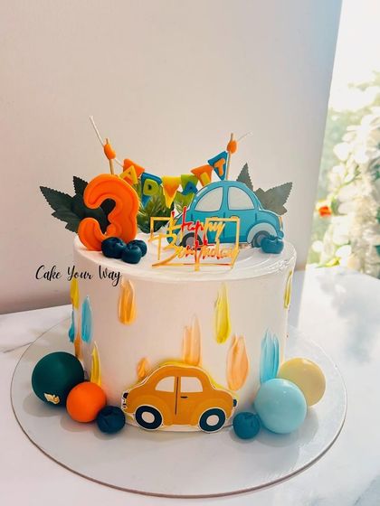 A vibrant and colorful car-themed cake for a 3rd birthday, with playful brushstrokes and fondant vehicles.