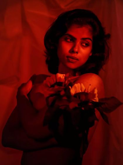 A wider shot that shows her holding the flowers protectively. Her expression is thoughtful, and the red light creates a dramatic, moody feel.