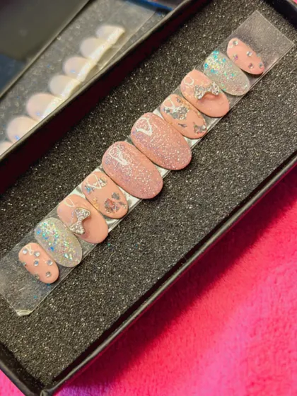 A playful and feminine press-on nail set in a rounded shape. It features a mix of glittery pink nails, nails with silver foil accents, and adorable 3D silver bows for a fun, textured look.