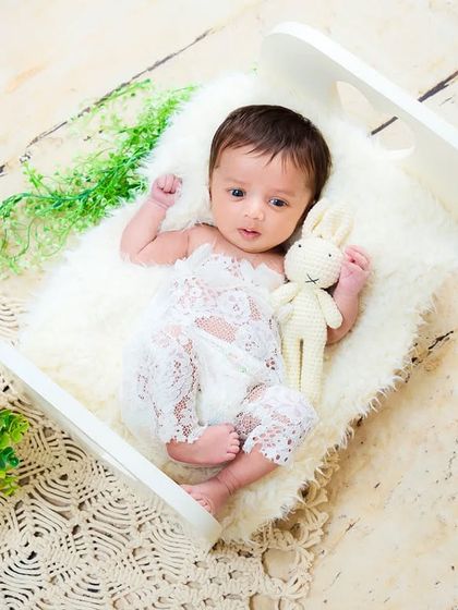 A newborn baby lies awake on a tiny white rocking chair, looking curious and content. This setup is perfect for capturing those early alert moments.