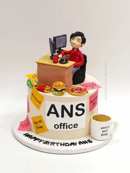 A cake for the "World's Best Boss," themed around a busy office desk, complete with a figurine, computer, sticky notes, and favorite snacks.