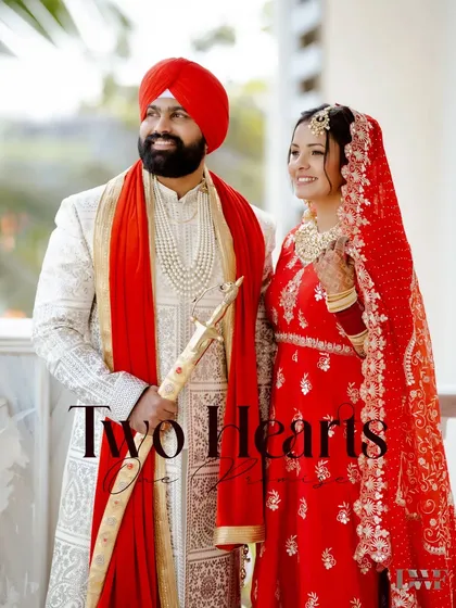 A regal portrait of a Punjabi couple in their traditional wedding attire, with the groom holding a kirpan.