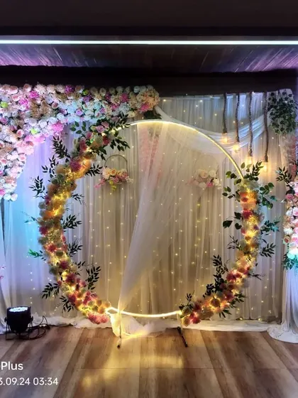 This engagement backdrop features a lit circular frame decorated with flowers and greenery. The design is asymmetrical for a more dynamic and modern visual appeal.
