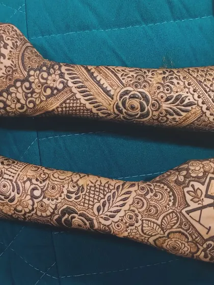 A full view of the arms, showing how the personalized initial designs on the palms are integrated into a complete, flowing bridal mehendi.