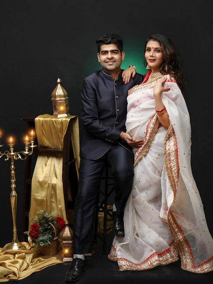 Nothing beats the beauty of an Indian woman in a saree. This elegant couple portrait features a stunning white and red saree, complemented by traditional props like lanterns and a candelabra.