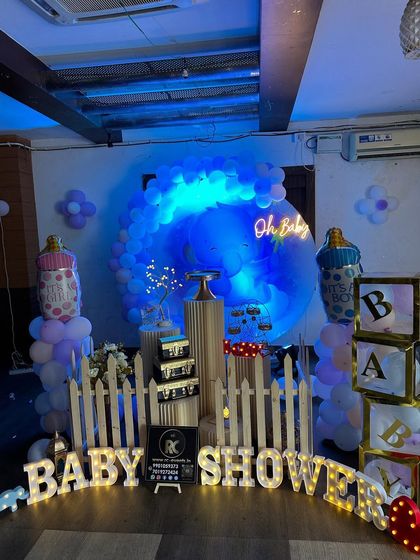 A baby shower setup with cool blue lighting and an "Oh Baby" neon sign. This decoration includes a circular balloon backdrop, marquee letters spelling "BABY SHOWER", and themed props like giant baby bottles.