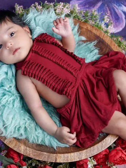 This two-month-old beauty is relaxing in a wooden bowl, dressed in a striking red outfit against a floral purple background.