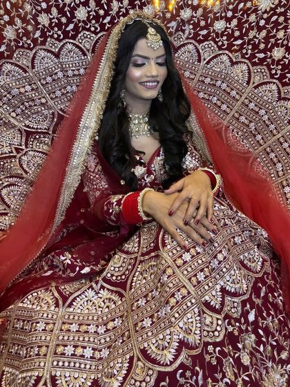 A beautiful shot of a model in a deep maroon lehenga. The smile is genuine, but the overall look is part of a styled shoot to showcase a complete bridal vision.