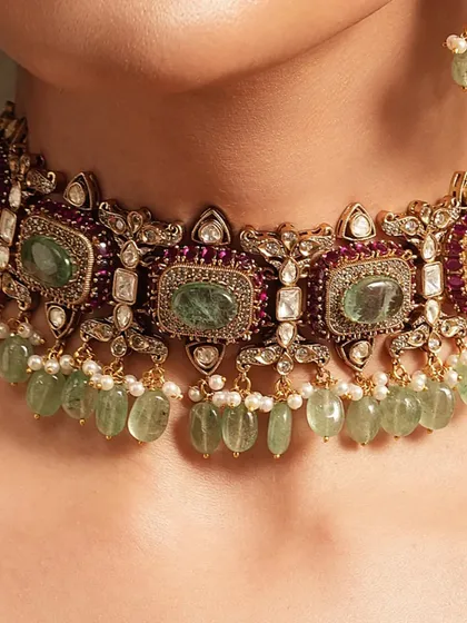 A close-up of a regal choker, showcasing the beautiful combination of emeralds, rubies, and uncut polki diamonds with delicate pearl drops.