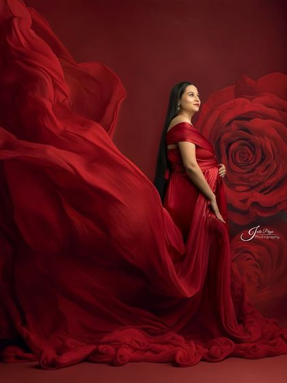 A variation of the fabric-tossing technique, this time against a rich red background with a subtle rose pattern. The mom-to-be looks up, creating a hopeful and elegant pose.