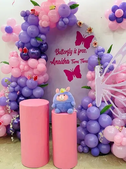 "Butterfly is free" theme for a third birthday. This setup features a purple and pink balloon arch, butterfly cutouts, and matching pink pedestals for a cohesive look.