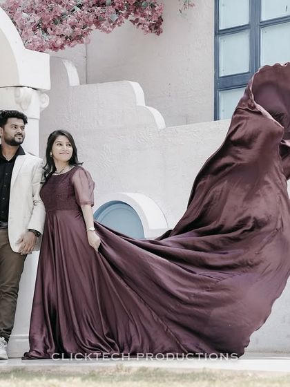 A couple walks hand-in-hand at an outdoor set, the bride's mauve trail gown flowing behind them, creating a sense of movement and romance.
