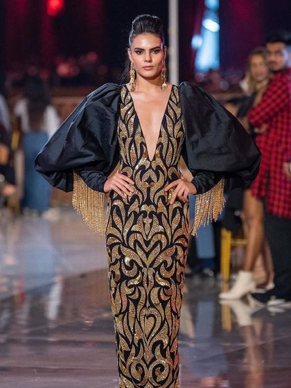 A full-length shot of a model on the runway for the Abu Jani Sandeep Khosla show. The makeup features a strong, defined eye and contoured cheekbones to match the dramatic gown.
