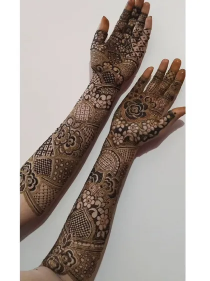 This full-arm design showcases a variety of patterns, from geometric grids on the wrist to floral work on the palm and fingers. It's a great example of a mixed-motif bridal style.