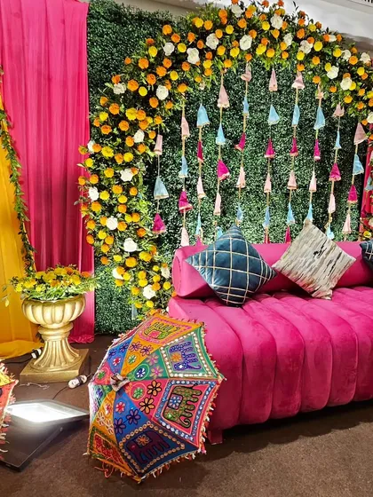 This vibrant Mehendi setup captures the joyful spirit of pre-wedding celebrations. We used a classic combination of bright pink and yellow drapes, a lush green wall with colorful tassels, and traditional Rajasthani umbrellas to create a festive photo corner.