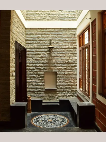 A quiet indoor nook with rough stone walls and a beautiful floor mandala, illuminated by a skylight, creating a perfect spot for contemplation.