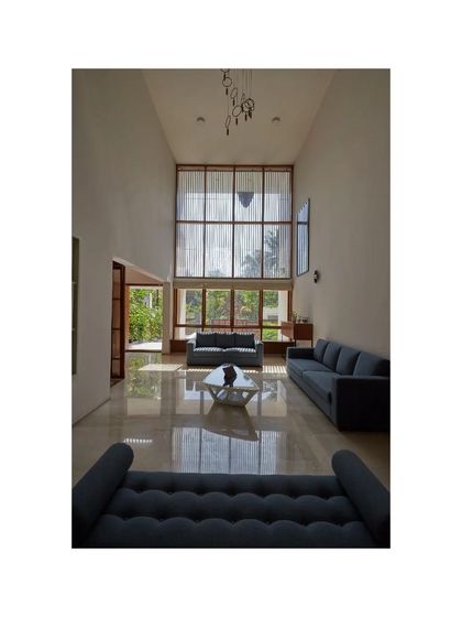 A wide shot of the living area in the Vikas Residence, showing the grand scale of the double-height space and the simple, elegant furniture arrangement.