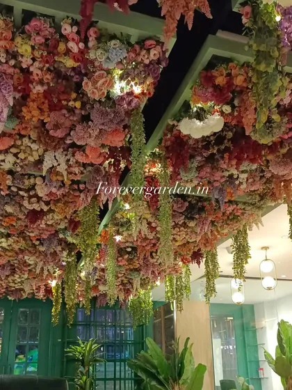An incredibly dense and colorful floral ceiling, packed with a variety of artificial flowers and hanging greenery, creating a fantasy garden feel for this venue.
