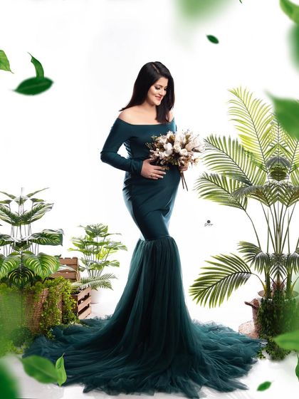 A beautiful portrait in a dark teal mermaid gown, surrounded by greenery. The added leaf effects create a lush, enchanted forest feeling for this maternity photo.