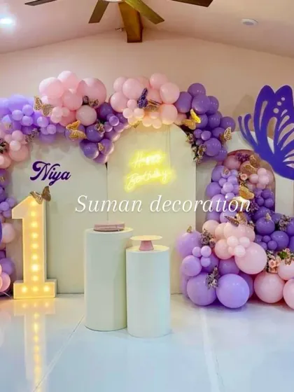 A beautiful butterfly-themed first birthday in shades of purple and pink. The decor features a large balloon arrangement, butterfly cutouts, a neon sign, and a light-up number '1'.
