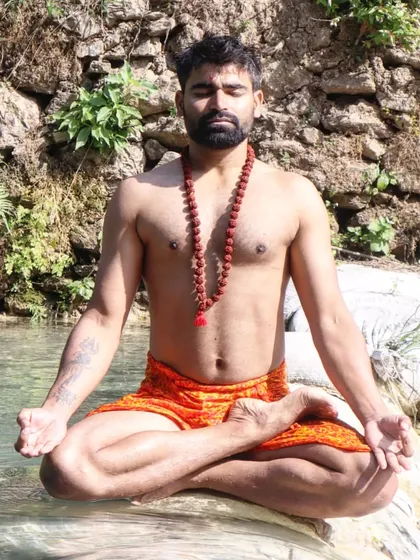 In Padmasana (Lotus Pose) by the water, wearing a Rudraksha mala. This traditional yogic posture and attire helps to create a sacred space for meditation, especially during auspicious times like Mahashivratri.