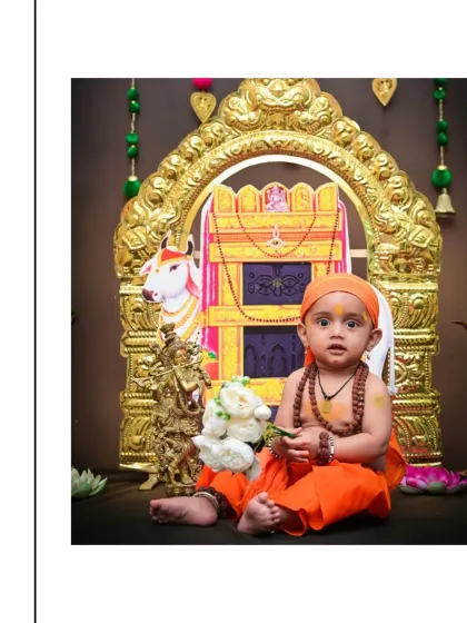 A baby boy dressed in orange robes sits before a golden shrine in this Raghavendra Swamy themed photoshoot. This is a beautiful way to honor faith and create a blessed memory.