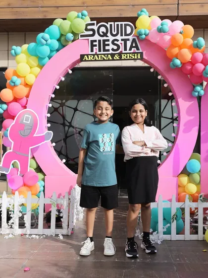 The birthday kids, Araina and Rish, posing at the entrance of their 'Squid Fiesta' party. I designed this custom circular entrance arch with colorful balloons and themed branding.