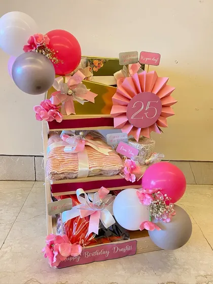 A birthday ladder for a 25th birthday, creatively displaying gifts on different tiers, decorated with pink balloons and a custom '25' sign.