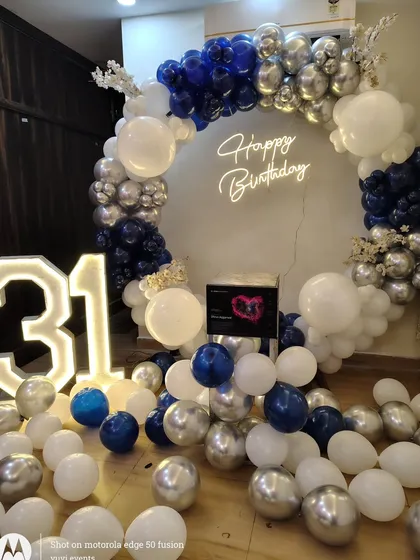 A stylish 31st birthday party decoration using a navy blue, silver, and white color scheme. The full balloon ring and light-up numbers create a fantastic photo opportunity.