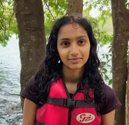 A young girl stands by the river, ready for her kayaking adventure at the Dandeli summer camp.