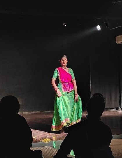 A striking green and pink costume illuminates the stage during a 'baithak' style performance. The intimate setting allows the audience to appreciate every detail.
