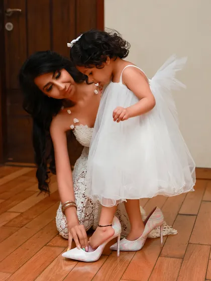 Little girls love playing dress-up in their mom's shoes. This is a classic, heartwarming moment captured during a lifestyle shoot at home, showing a daughter wanting to be just like her mom.
