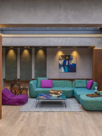 This vibrant lounge in a New Delhi residence was designed as a lively entertainment area. The space features eclectic Paola Lenti furniture set against concrete and rust-finished walls, with a retractable roof that creates a seamless connection to the outdoors for an open-air experience.