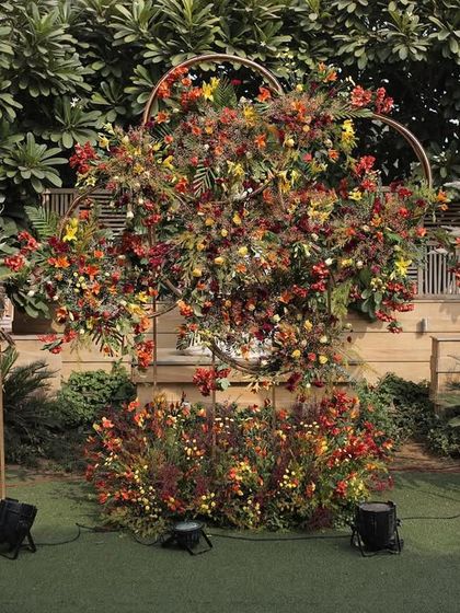 A photo backdrop inspired by the colors of autumn, featuring a heart-shaped frame filled with rustic, warm-toned florals and pampas grass.
