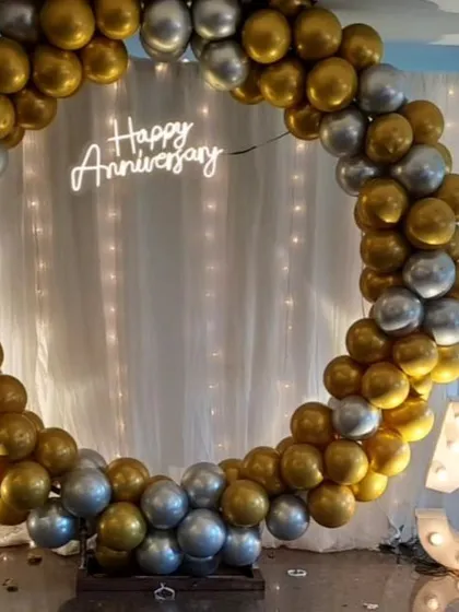 We celebrated 50 golden years with this elegant anniversary party setup. The highlight is a large circular balloon frame in gold and silver, a "Happy Anniversary" neon sign, and marquee numbers, creating a perfect photo booth for the happy couple and their guests.