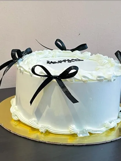 Embracing the trendy "coquette" aesthetic, this elegant white cake is adorned with delicate piping and simple black bows for a chic and fashionable look.