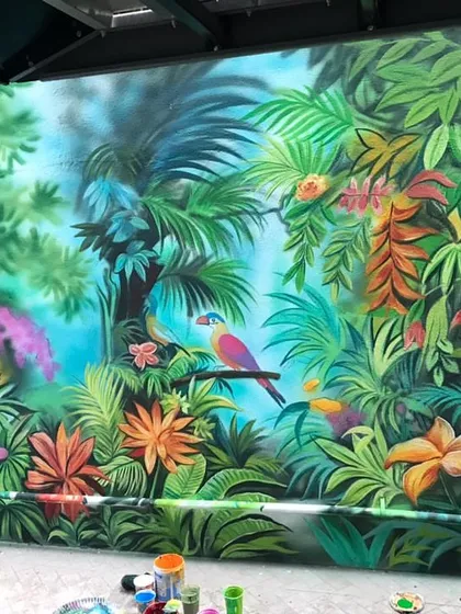 The forest mural coming together with vibrant colors and lush details, including tropical birds and exotic flowers.