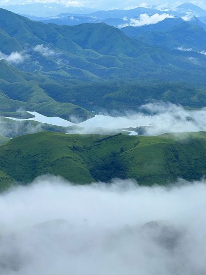 A stunning view of the Lakya Dam backwaters from the Gangadikal peak, with clouds floating below.
