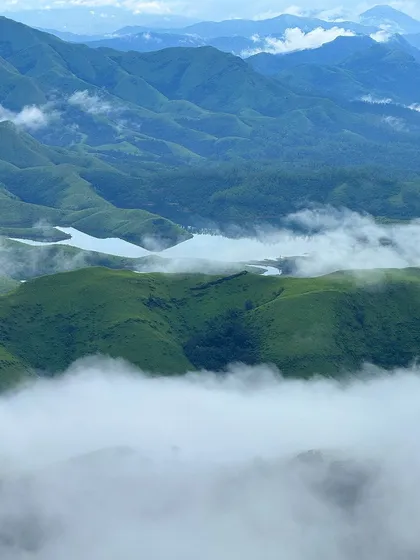 A stunning view of the Lakya Dam backwaters from the Gangadikal peak, with clouds floating below.