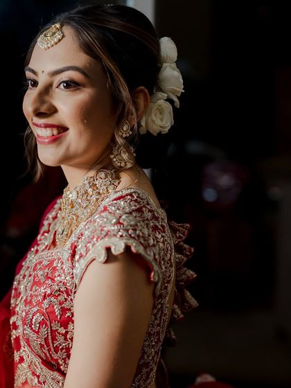 A side profile showcasing the elegant hair updo adorned with white roses. The makeup is fresh and radiant, with a bright smile that completes the look.